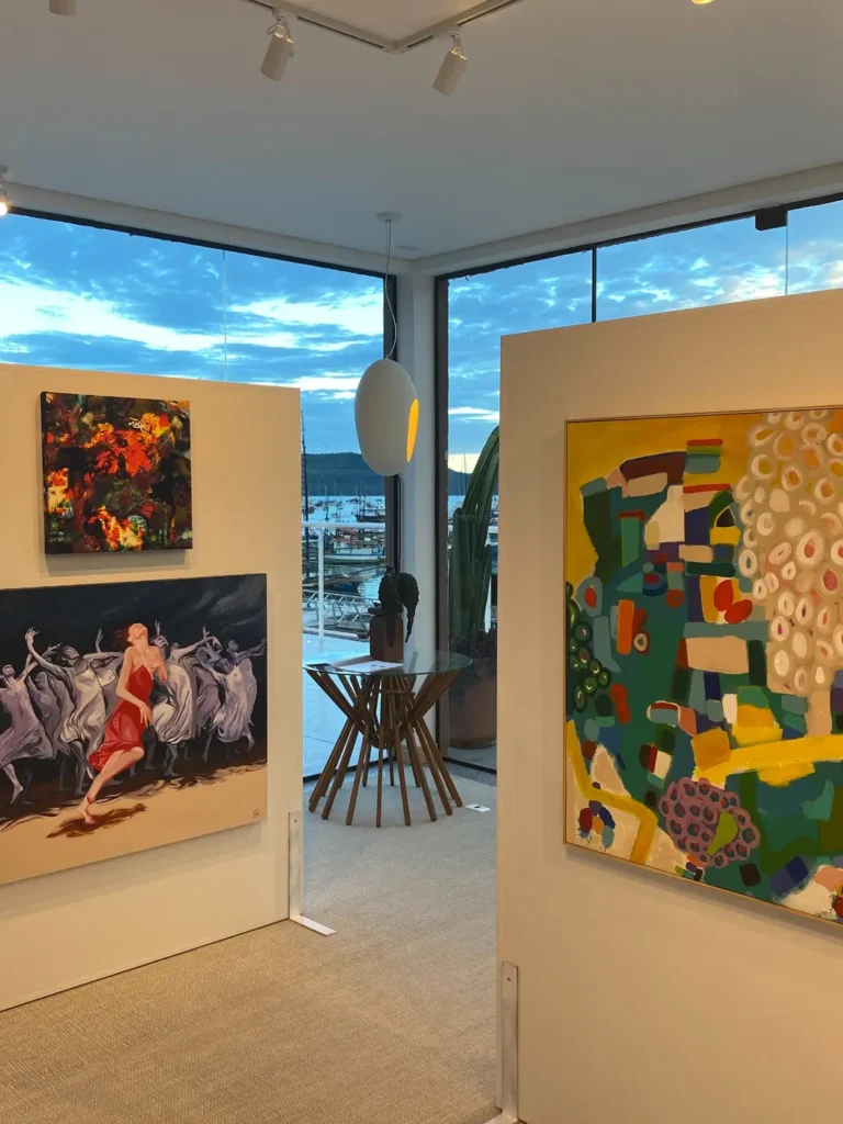 Exposição Reflexões na AGaleria Ubatuba, com obras de diferentes artistas e vista para a marina do Saco da Ribeira.