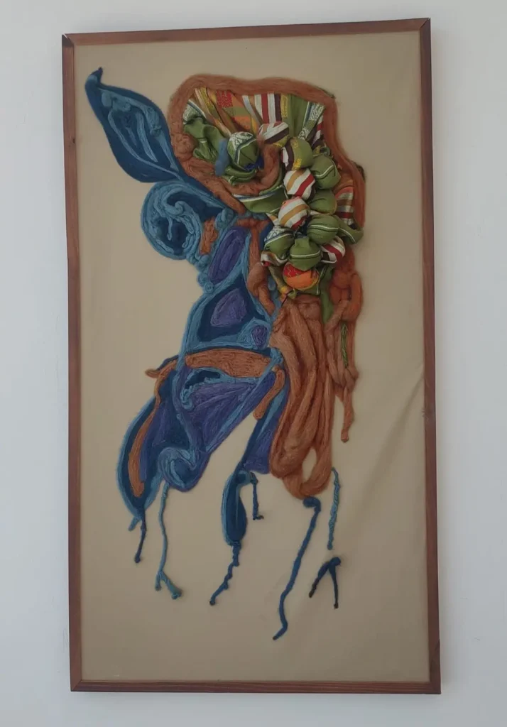 Obra têxtil Raízes, de Regina Helene, criada com lã merino e tecido étnico equatoriano em tons de azul, verde e terracota.