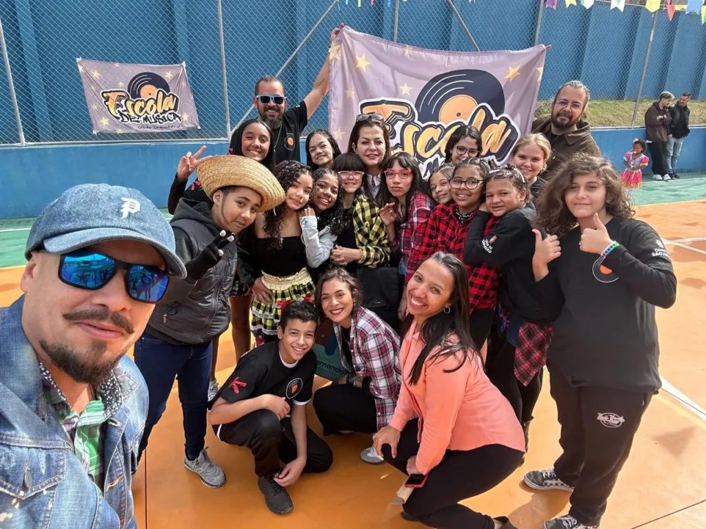 Grupo de participantes do projeto Capão–Congonhas reunido em uma quadra, diante das faixas da Escola de Música