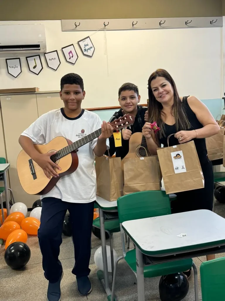 Dois estudantes com violões e uma mulher posam em sala de aula do projeto Capão–Congonhas.