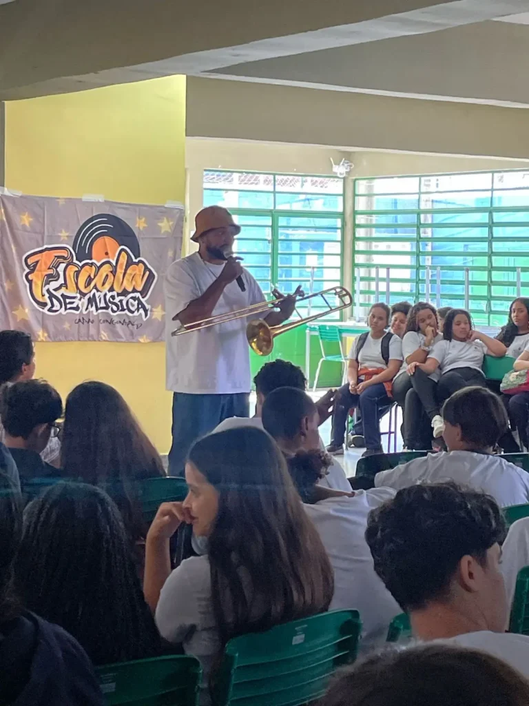 Músico apresenta um trombone a estudantes durante atividade do projeto Capão–Congonhas em sala de aula.