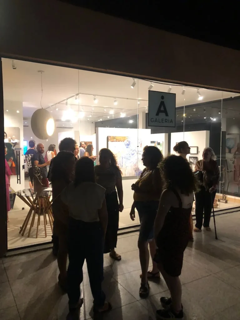 Público reunido em exposição da AGaleria Ubatuba, com obras de arte ao fundo.