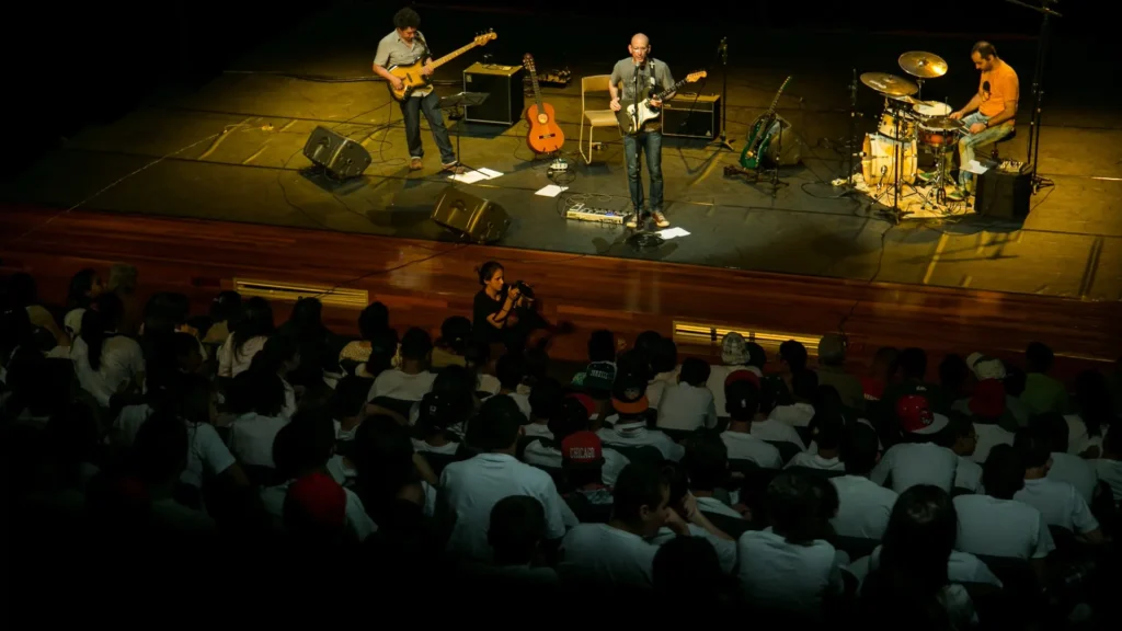 Apresentação do projeto Tarde Instrumental para uma plateia de estudantes, com músicos no palco.