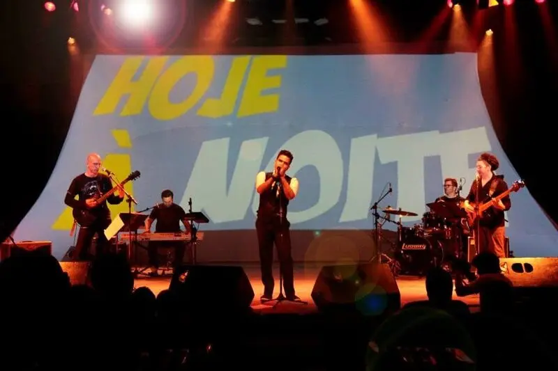 Pedro Lobo canta com sua banda diante da projeção Hoje à Noite no palco.